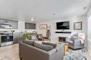 A modern living room with a sofa, a television, and a kitchen area with cabinets and appliances.