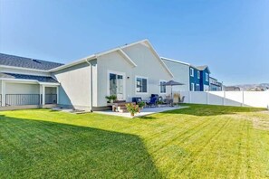 Una moderna casa a due piani con un prato curato, un patio con mobili da esterno e un cielo sereno.