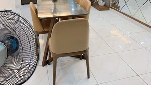 Un espace repas moderne avec une table en verre, des chaises de couleur beige et un grand ventilateur.