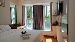 Une chambre d’hôtel avec un grand lit, une table de chevet avec une lampe, un téléviseur fixé au mur et une fenêtre avec des rideaux.