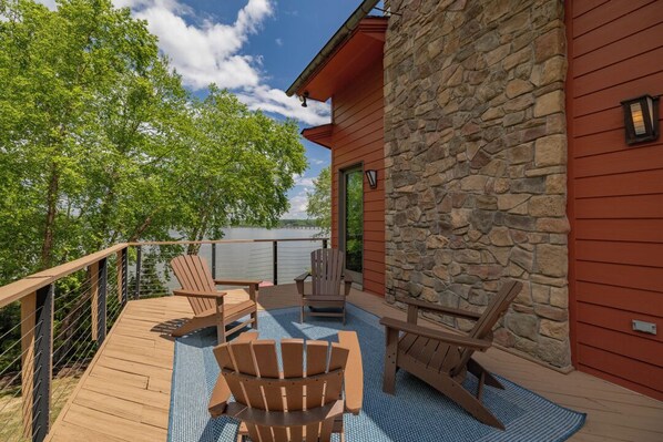 A wooden deck with Adirondack chairs, a stone wall, and a view of trees.