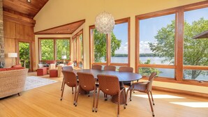 A spacious dining area with a large table and wicker chairs, large windows with a lake view, and a wooden ceiling. - Graceland (Clarksville)