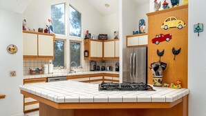 A kitchen with a central island, wooden cabinets, a stainless steel refrigerator, and a window overlooking a garden.