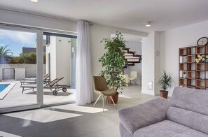 Una sala de estar moderna con un sofá gris, una planta grande en maceta y una estantería de madera.