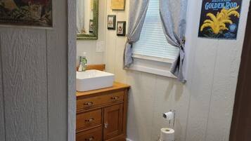 A bathroom with a wooden vanity, a toilet, a rug, and a framed poster on the wall.