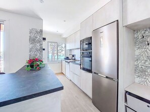 Una cocina moderna con horno empotrado, refrigerador y ventana con vistas a árboles.