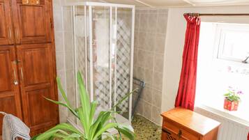 A bathroom with a shower, a wooden cabinet, a plant, and a window with a red curtain.