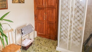 Un baño con armario de madera, cabina de ducha, una silla y una planta.