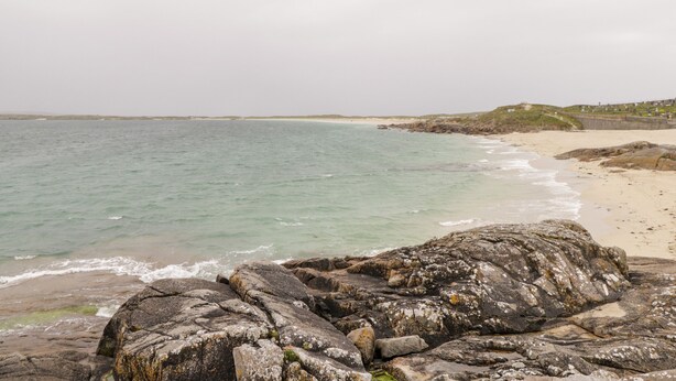 Una playa rocosa con aguas claras, una orilla arenosa y una vista distante de un pueblo.