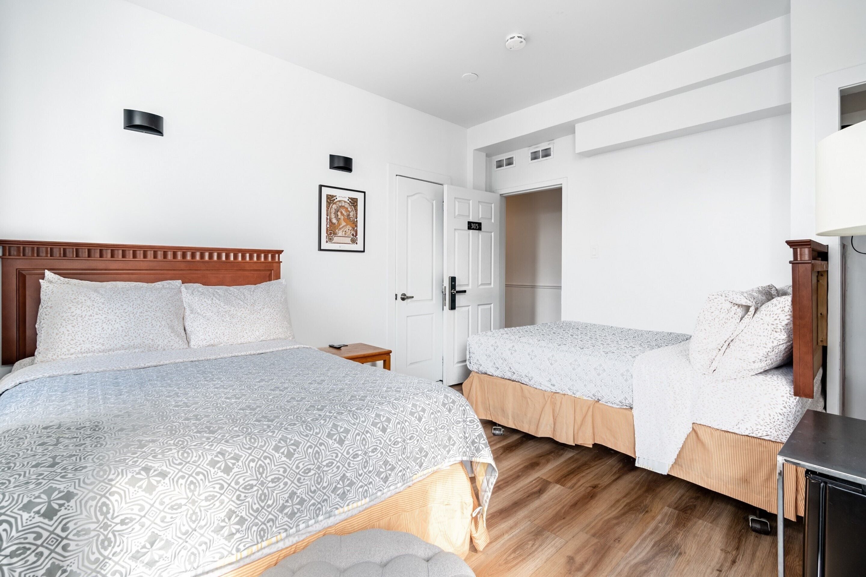 Ein Hotelzimmer mit zwei Betten, einem hölzernen Kopfteil, einem kleinen Nachttisch, einem Kleiderschrank und einer Tür zu einem weiteren Raum.