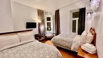 Habitació d'hotel amb dos llits, una televisió, escriptori amb làmpada, una cadira i finestra amb cortines.