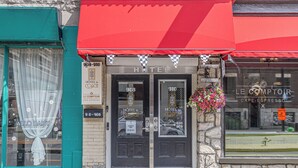 A hotel entrance with a red awning, two doors labeled '908' and '910', and a flower basket hanging on the right. - Hotel le Coach (Montreal)