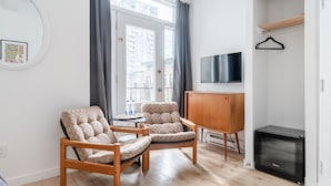 A modern living room with two beige armchairs, a small round table, a TV mounted on the wall, and a wooden cabinet. - Hotel le Coach (Montreal)