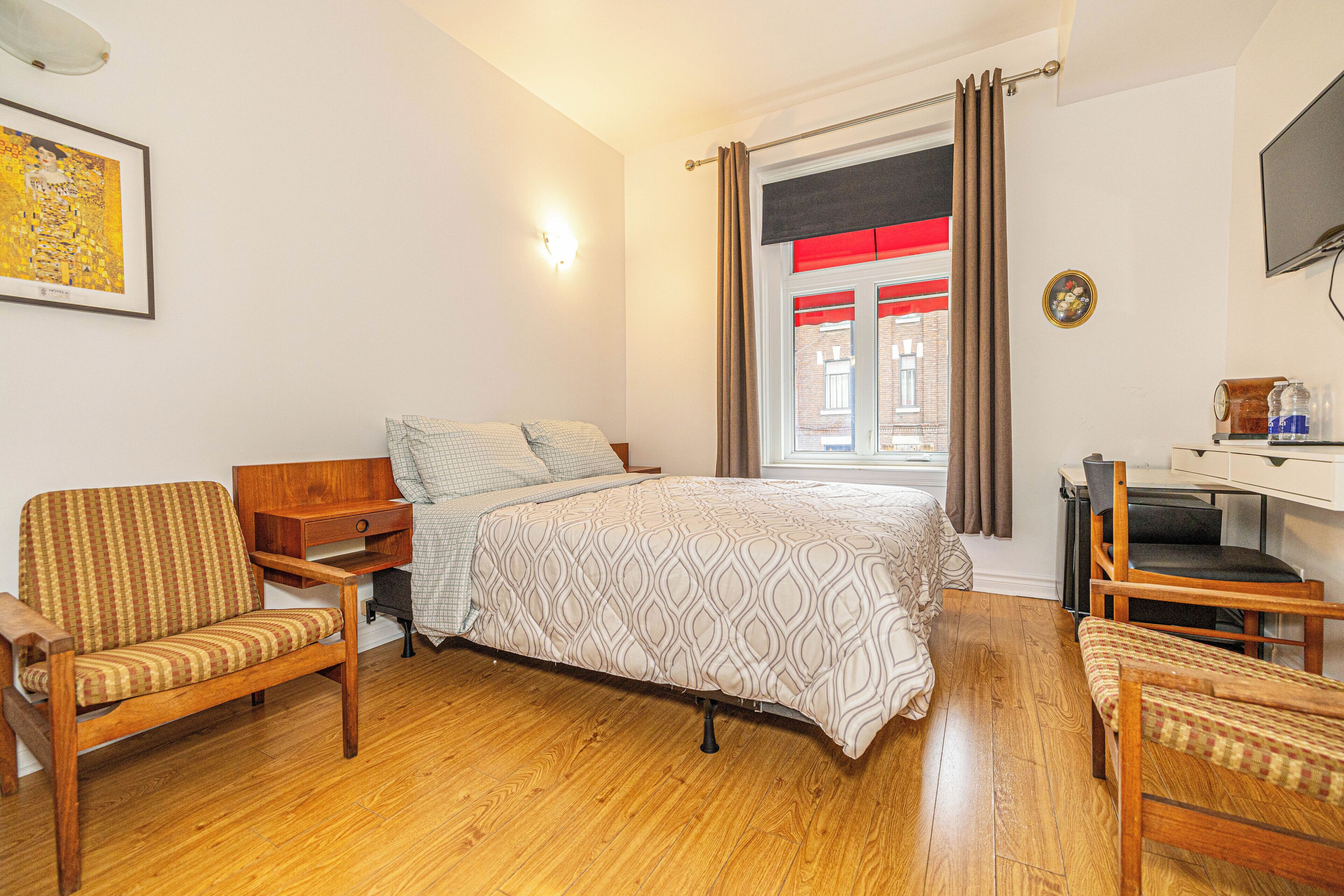 A bedroom with a bed, a wooden chair, a desk, and a window with curtains.