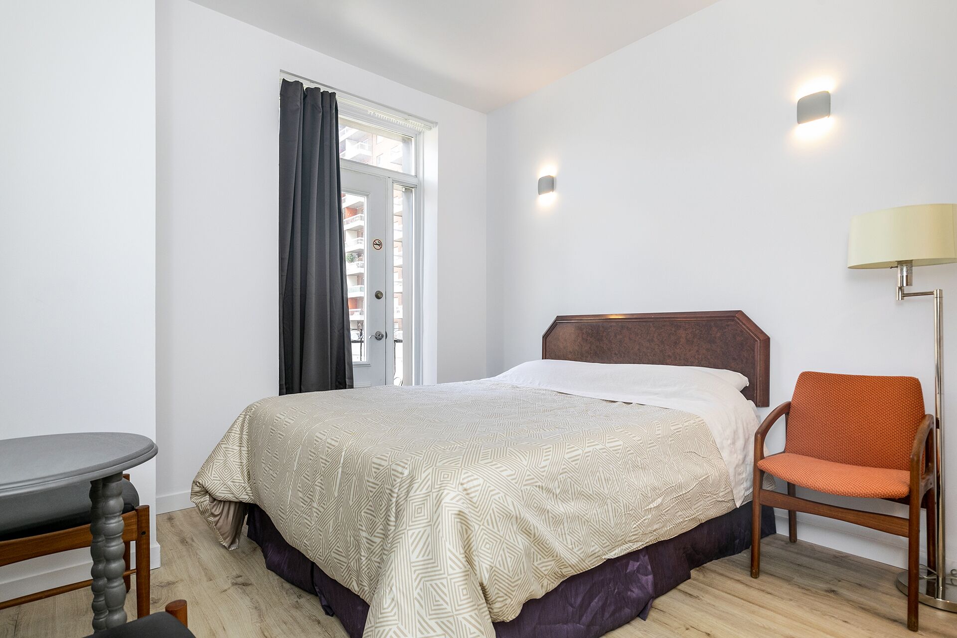 A hotel room with a bed, a chair, a table, and a window with curtains.