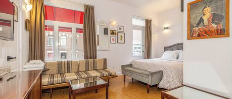 Una habitación de hotel con sofá, cama, mesa de centro de vidrio y escritorio de madera.