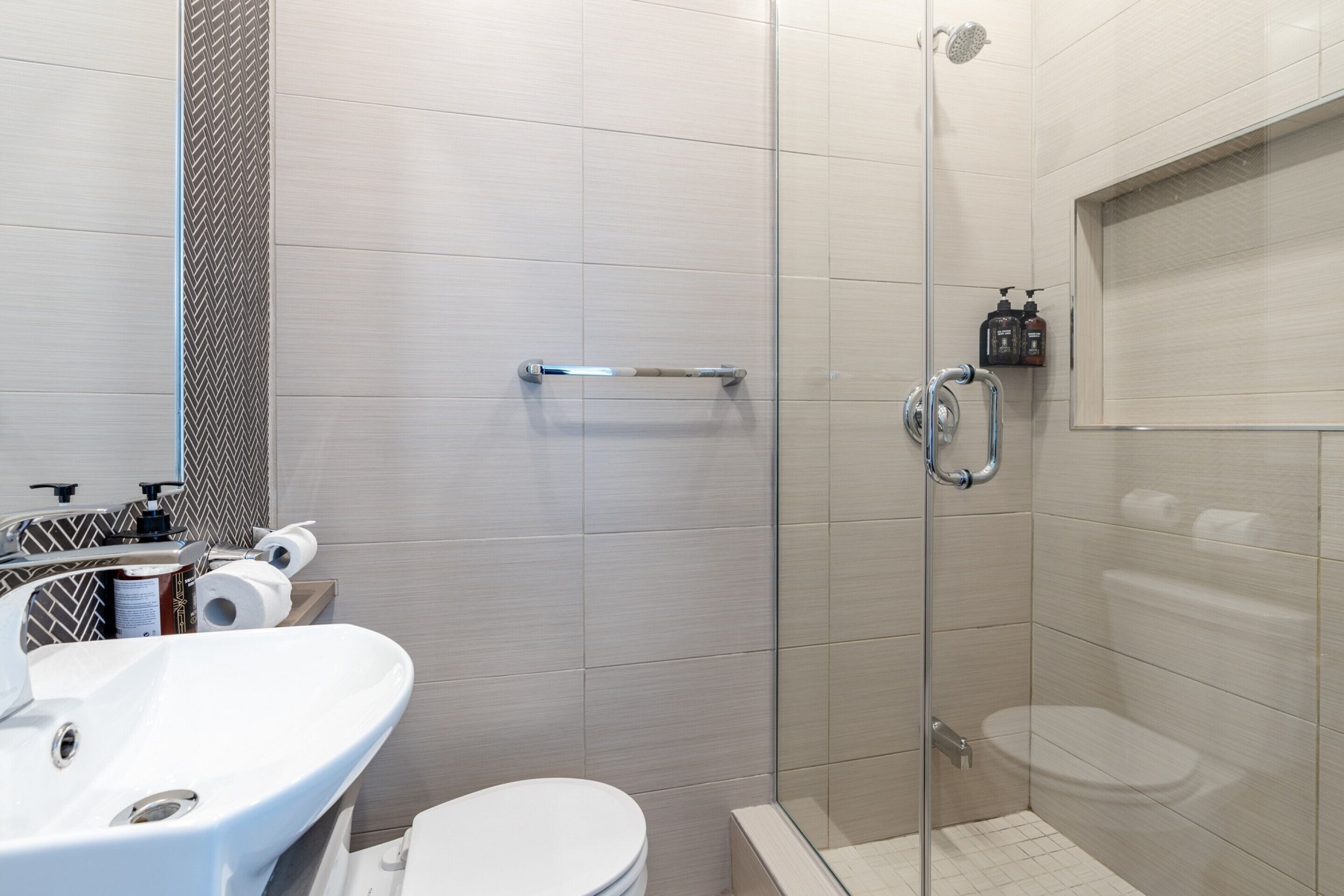 A modern bathroom with a glass shower enclosure, a white sink, and a toilet.