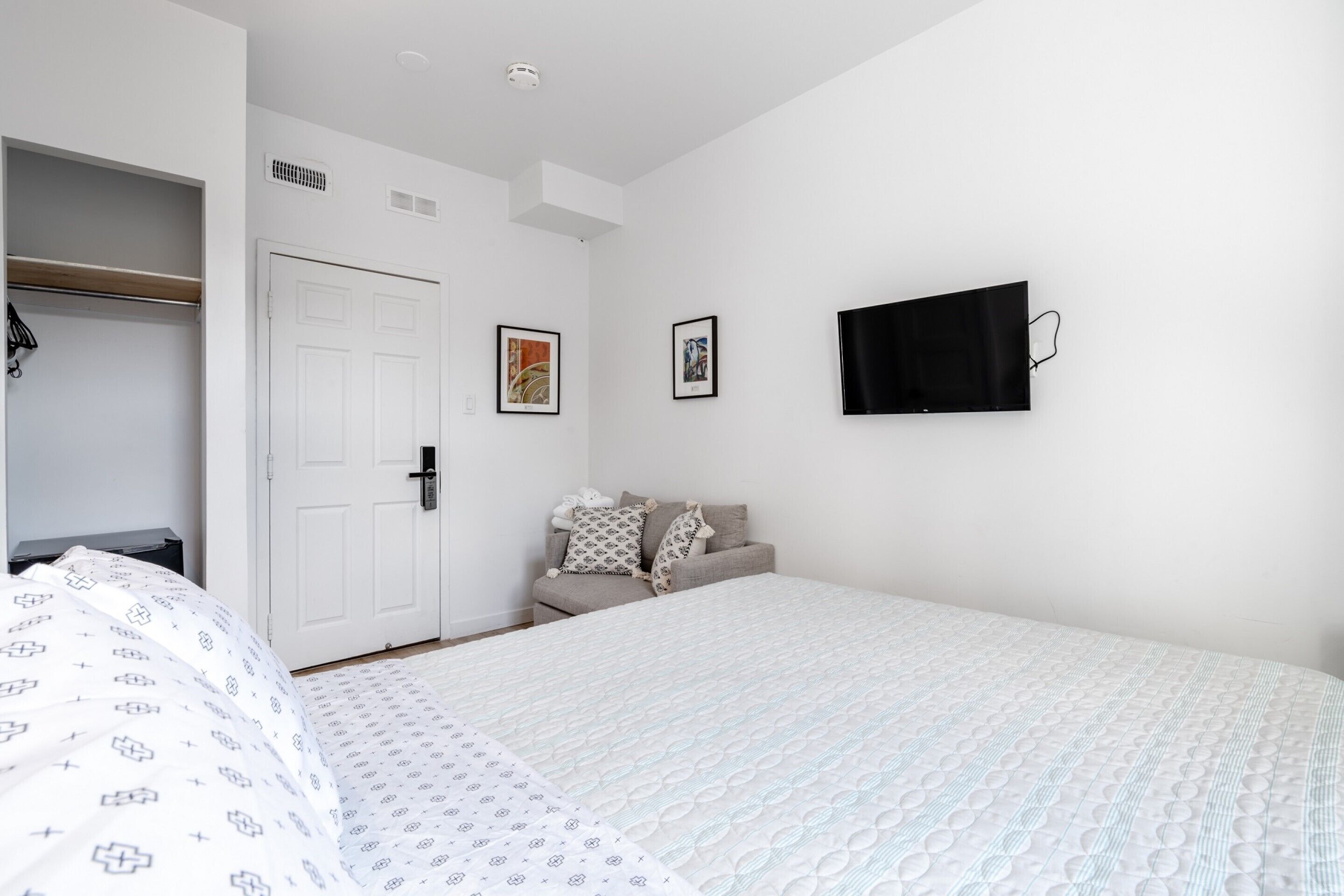 Un dormitorio con cama, armario, sofá y televisión en la pared.