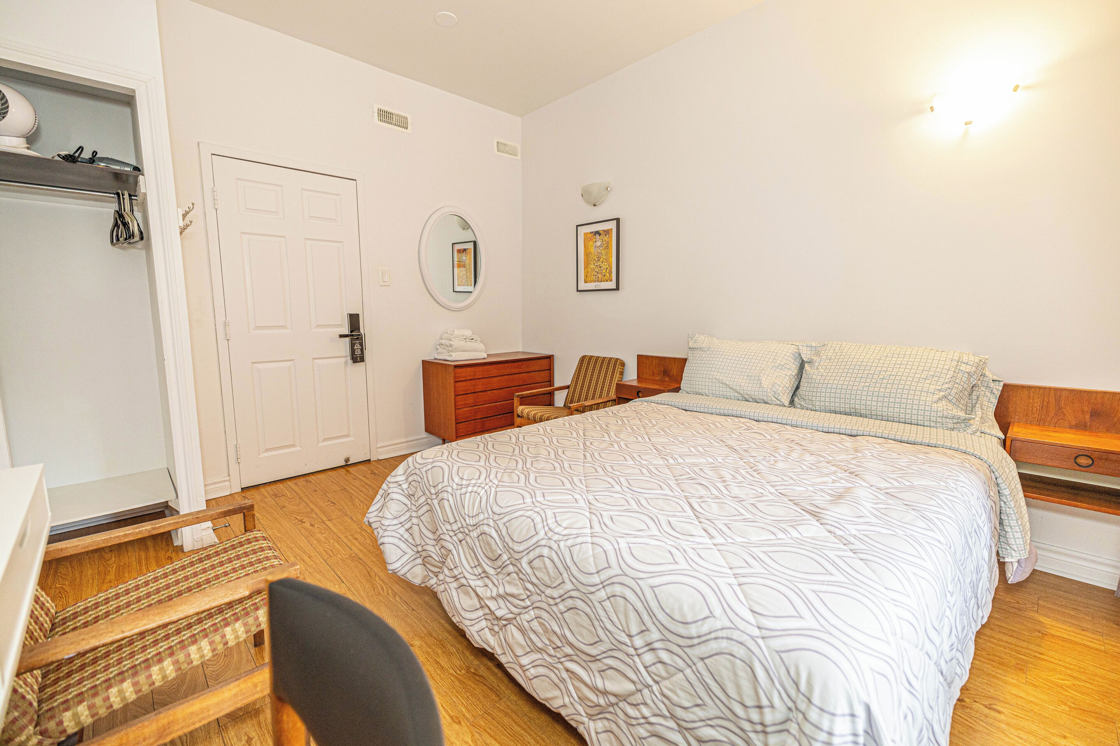 A bedroom with a bed, a dresser, a chair, a wardrobe, and a mirror.