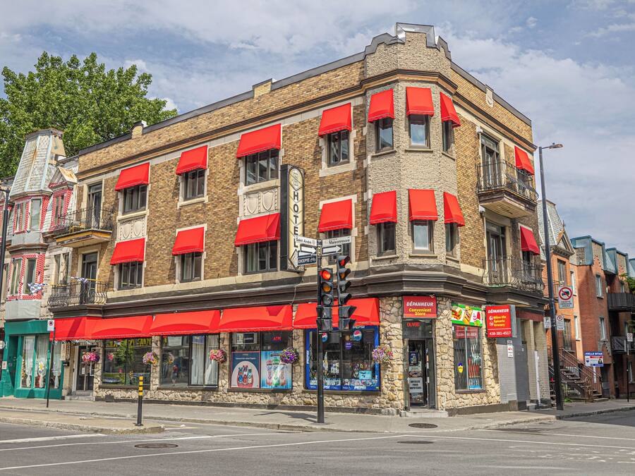 Un edificio en esquina con toldos rojos, un cajero automático visible y un letrero de hotel.