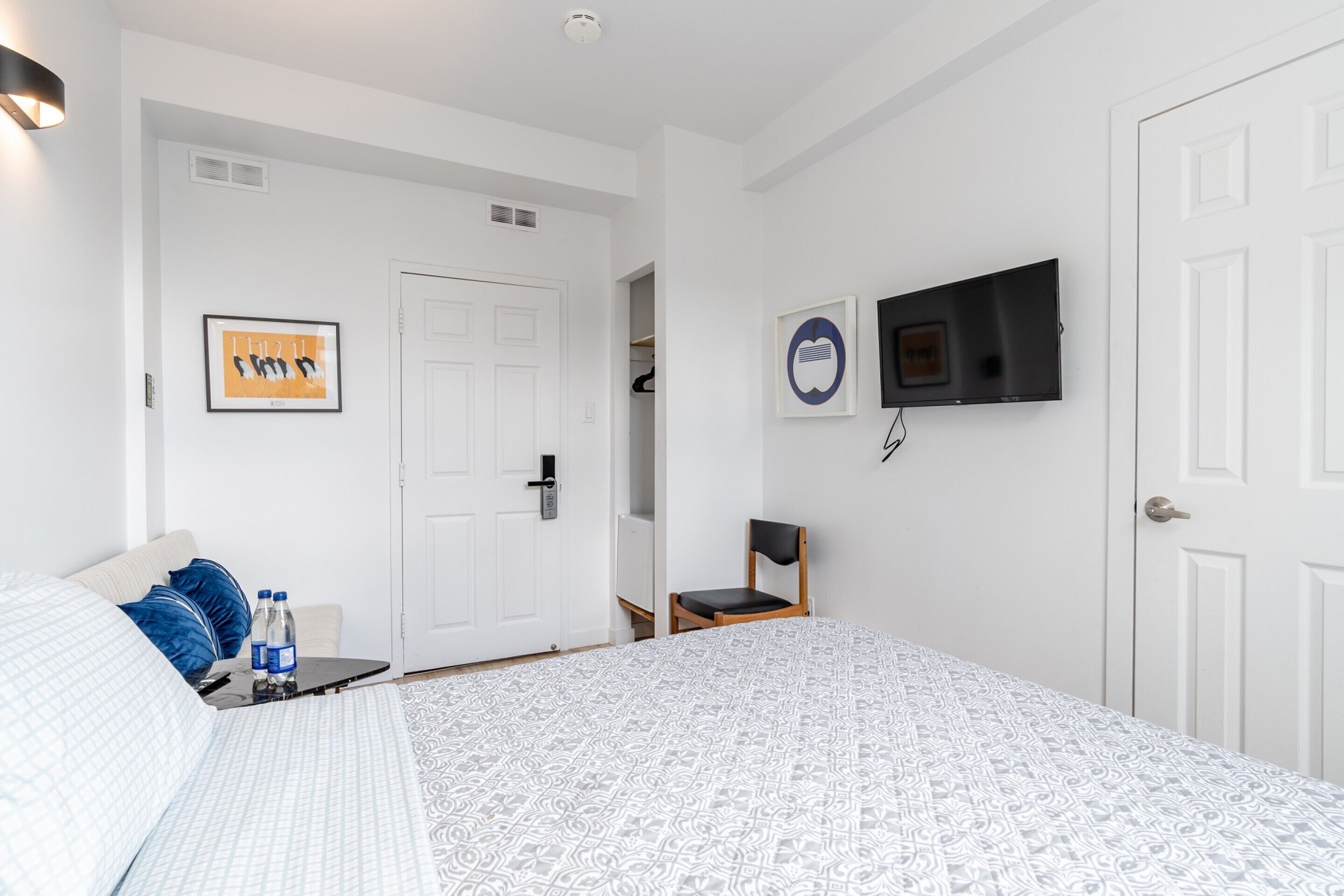 A hotel room with a bed, a TV mounted on the wall, a door, and a small table with a chair.