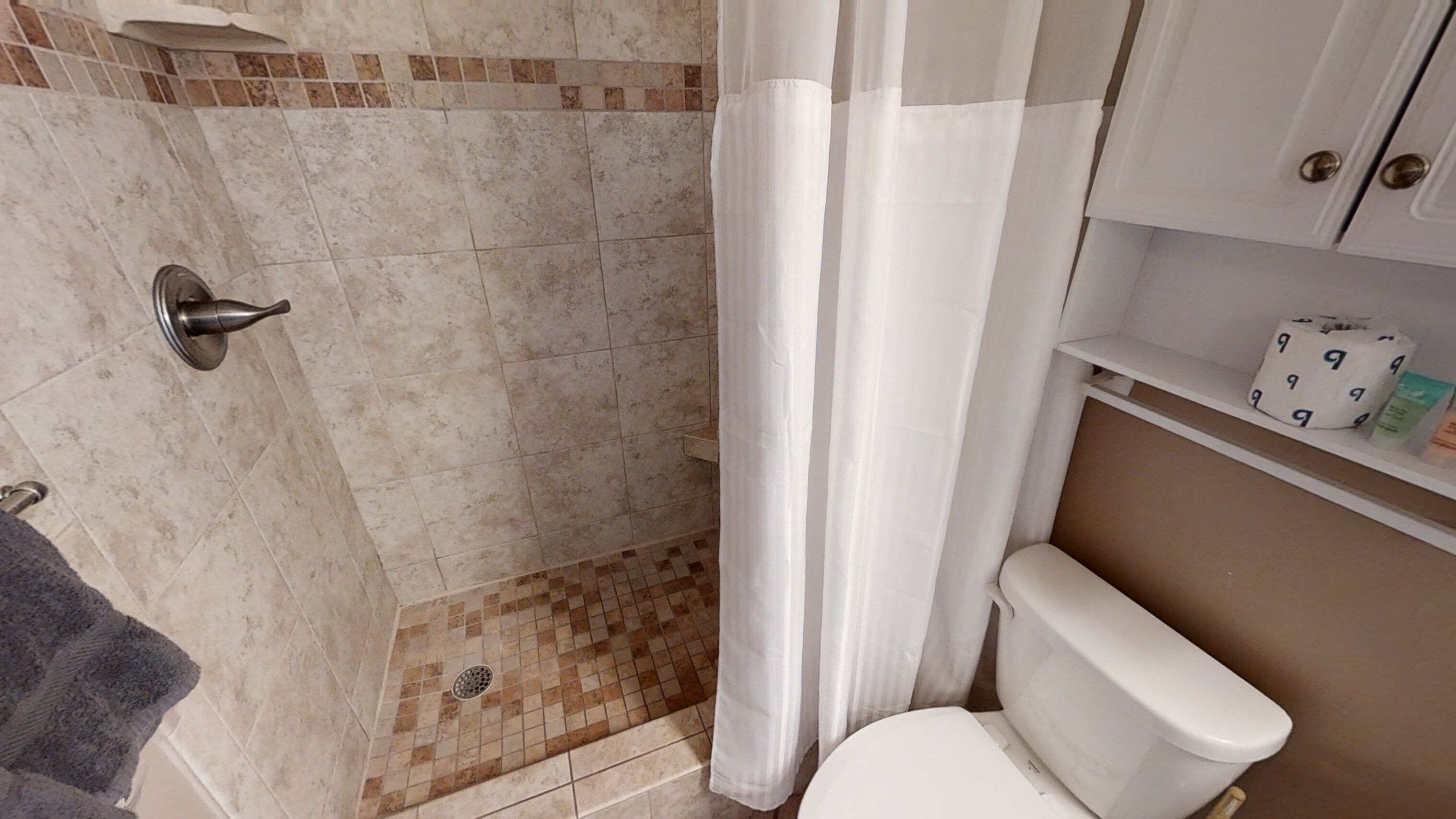 Ein Badezimmer mit Dusche, Toilette und Ablagen für Pflegeprodukte.