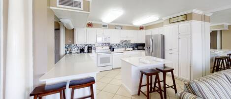 A modern kitchen with white cabinetry, a central island with stools, and a dining area with striped cushions.