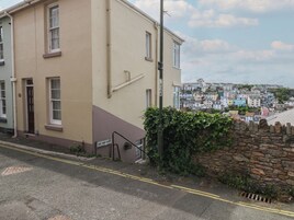 Una calle residencial con un edificio color crema, un muro de piedra y una vista de casas coloridas al fondo.