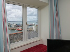 Una habitación con ventana que da a un puerto, un banco rojo y un televisor.