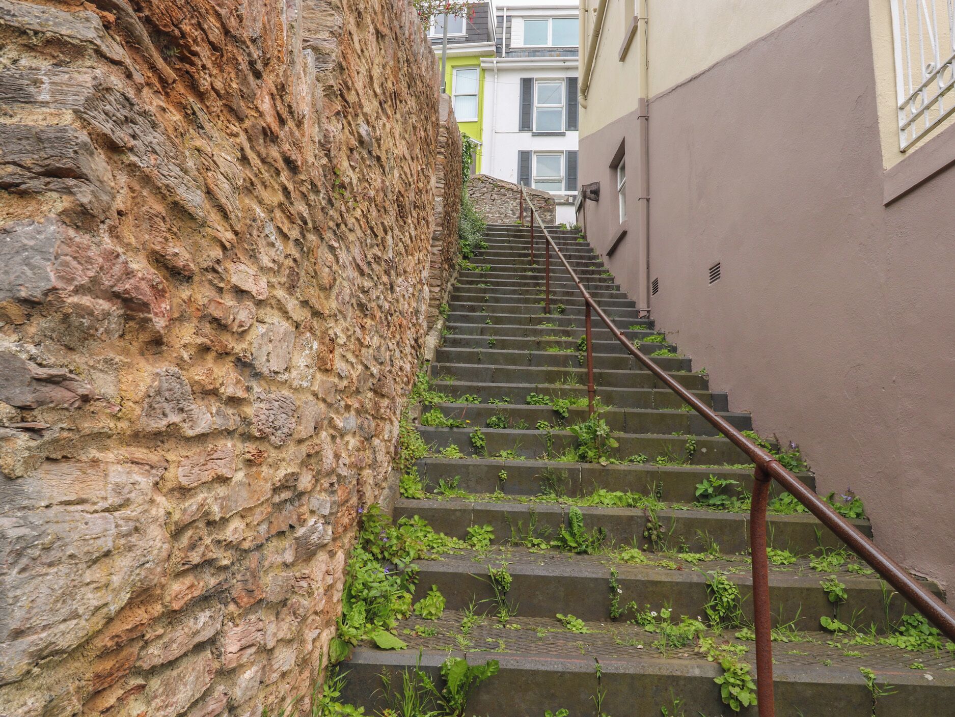 A staircase with stone walls on one side and a building on the other, leading to an upper floor.