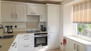 A modern kitchen with white cabinetry, a built-in oven, and a window with a striped blind. - Bay View (Brixham)