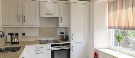 A modern kitchen with white cabinetry, a built-in oven, and a window with a striped blind.