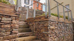 Eine Steintreppe mit Metallgeländern, die zu einem Holzdeck mit Pflanzen führt.