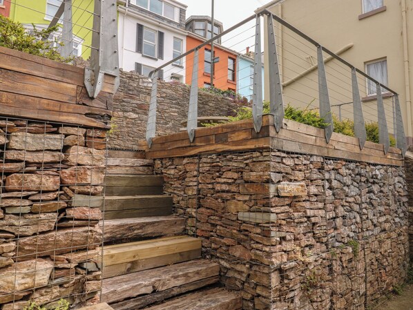 Un escalier en pierre avec des rampes métalliques, menant à une terrasse en bois agrémentée de plantes.