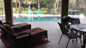 A poolside area with lounge chairs and a table, overlooking a swimming pool and a garden with chairs and umbrellas. - RELAXING OASIS-Private Lanai Heated POOL & SPA.  4 Bed, 3.5 Bath / Beach 10 min (Bonita Springs)