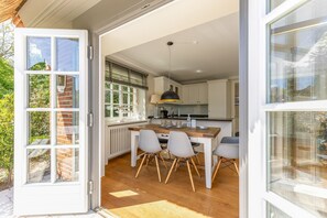 Une cuisine avec un coin repas, des meubles blancs, une table en bois et un luminaire suspendu.