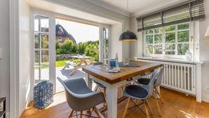 Un comedor con mesa de madera, sillas, una lámpara colgante y vista a una casa a través de una puerta de vidrio.