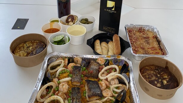 Une table dressée avec divers plats, notamment une paella aux fruits de mer, du pain et des sauces.