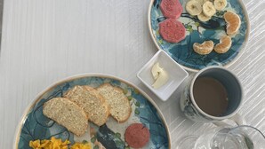 Une table dressée pour le petit-déjeuner, avec des œufs brouillés, des tranches de saucisse, des toasts, des bananes et une tasse de café.