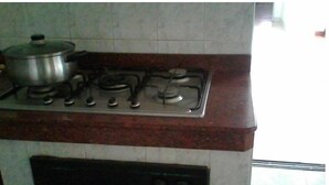 Une cuisine équipée d’une cuisinière à gaz, avec une casserole sur le brûleur de gauche et un dosseret carrelé.