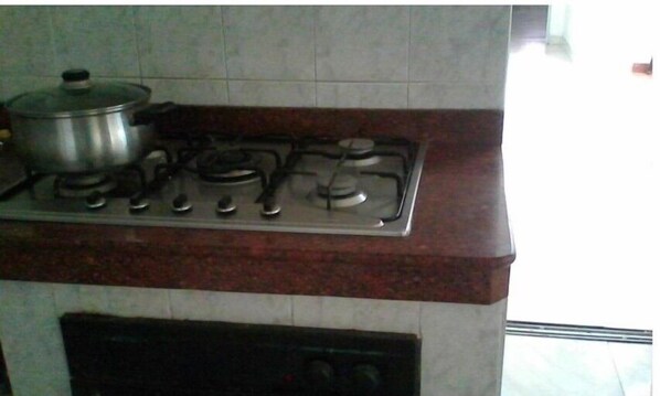 A kitchen with a gas stove, a pot on the left burner, and a tiled backsplash.