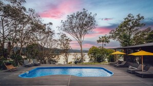 A wooden deck with a swimming pool, lounge chairs, and yellow umbrellas. - Marramarra Lodge (Berowra Waters)