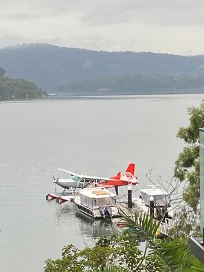 A lake with two seaplanes docked at a pier, surrounded by greenery and mountains in the background. - Marramarra Lodge (Berowra Waters)