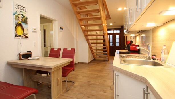 A kitchen with a wooden staircase, a dining area with red chairs, and a kitchen counter with a sink.
