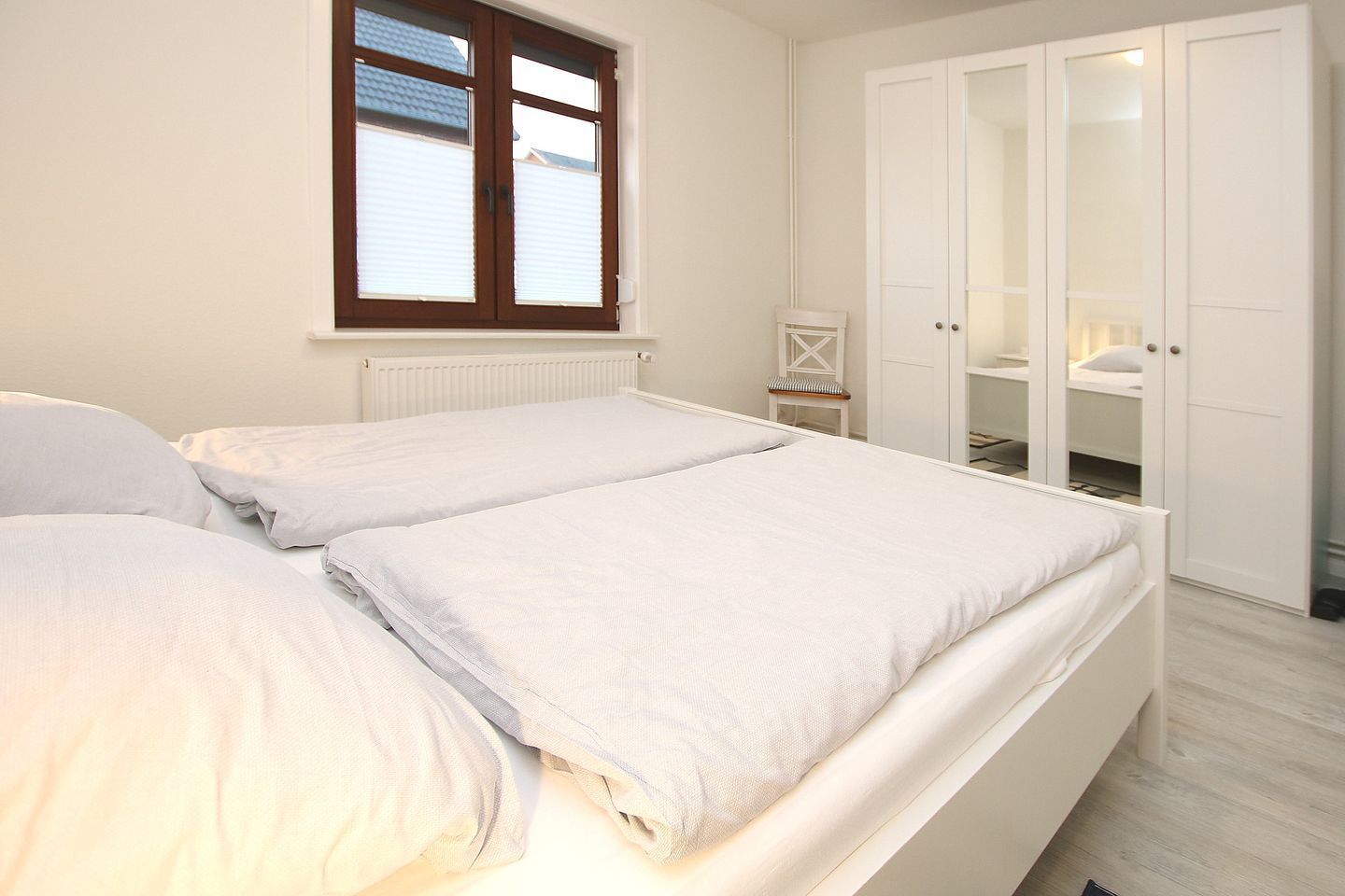 Een slaapkamer met twee bedden, een raam, een radiator, een kledingkast en een klein tafeltje.