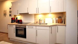 A compact kitchen with white cabinets, a built-in oven, a sink, and a coffee maker.