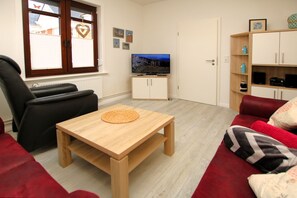 A living room with a TV, a wooden table, a red sofa, and a black leather chair. - Badestraße 7 - Historic townhouse with approx. 80m² living space with room for 4 (Wyk auf Föhr)