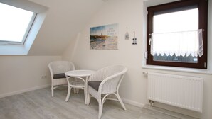A room with a skylight, a table with two chairs, a radiator, and a window with a curtain.