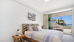 Ein Schlafzimmer mit einem großen Bett, einem Nachttisch, einem modernen Wandbild und einem Balkon mit Meerblick.