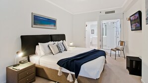 Ein Schlafzimmer mit Bett, Nachttischen, einem Sessel und einer Tür zum Badezimmer.